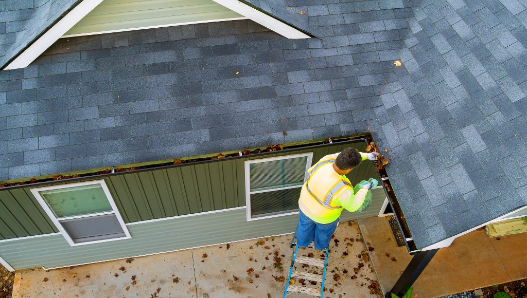 A roofing expert clears clogged gutters on a fall morning
