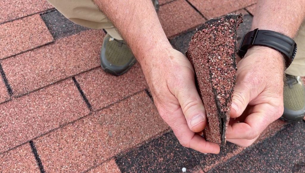 A roofer demonstrates the brittleness of dry shingles by bending one in half until it cracks.