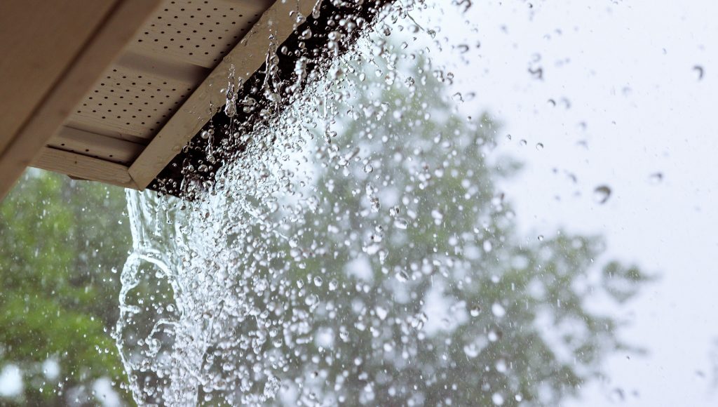 Heavy rain pouring from a roof's gutters during a rainstorm.