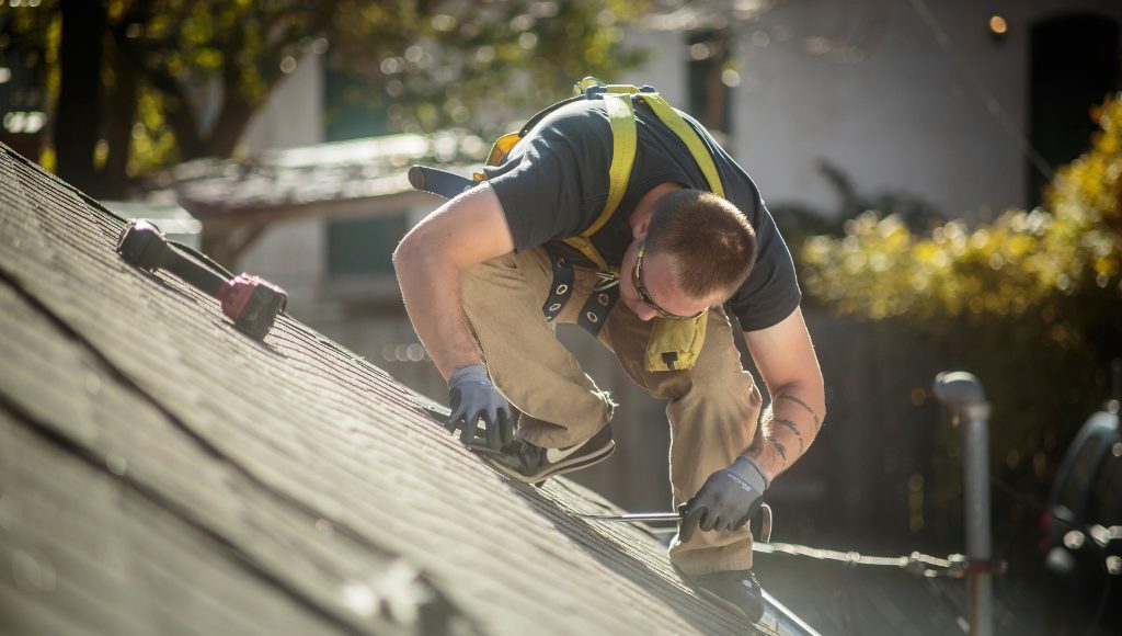 A roofer fixes an asphalt shingle roof on a sunny day.