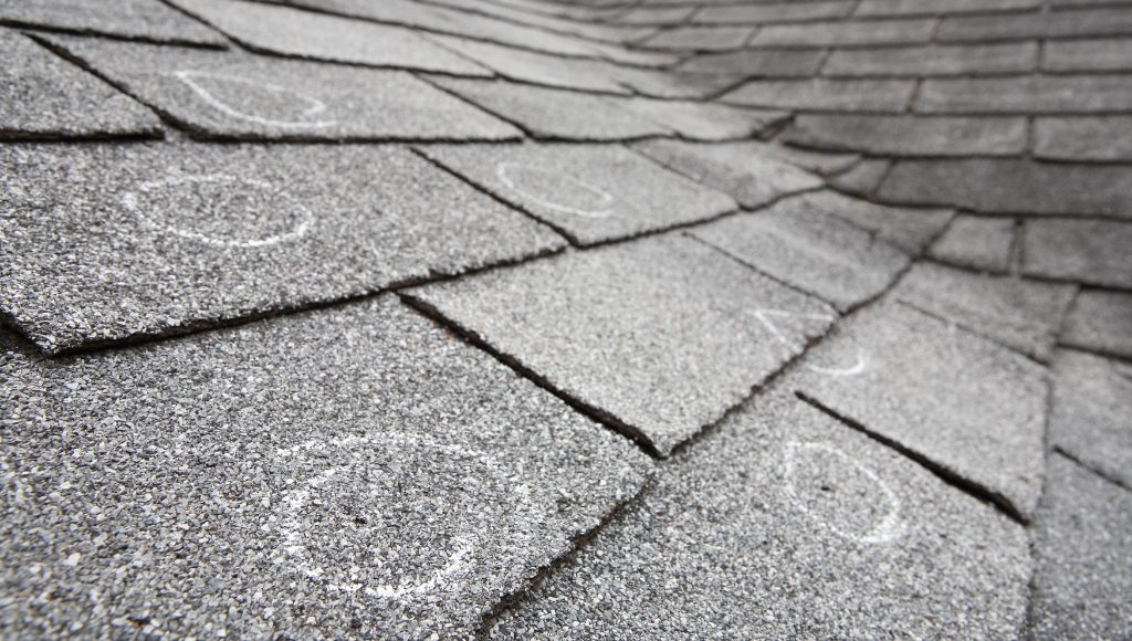 Old roof with hail damaged shingles, chalk circles mark the damage.