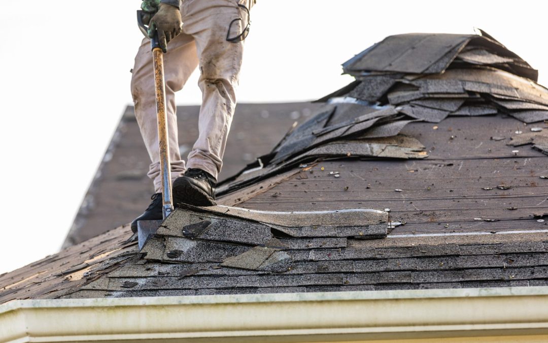A roofer is removing damaged sections of shingles with a shovel.