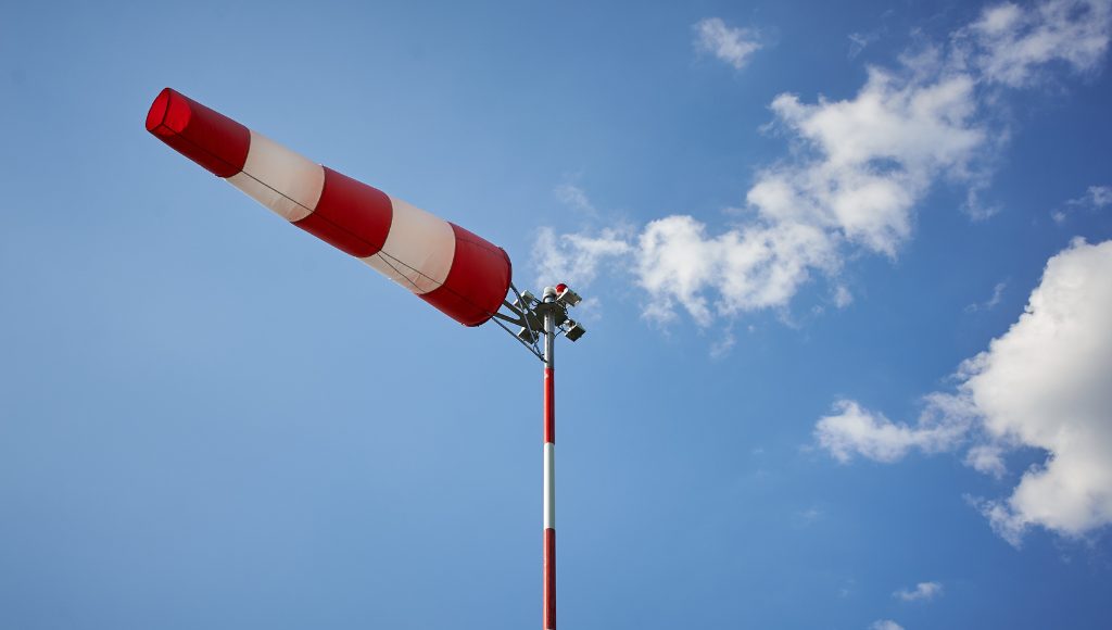 A red and white wind sock sticking straight out to the side against a blue sky, indicating strong winds.