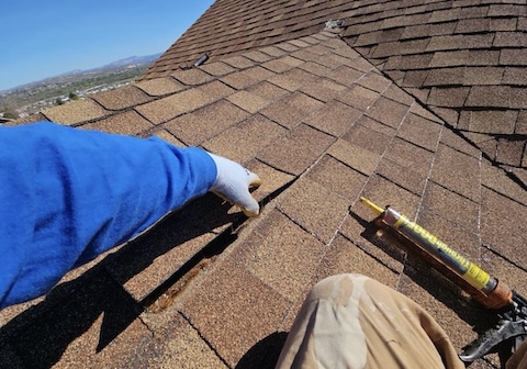 Worker on an asphalt shingle roof doing repairs