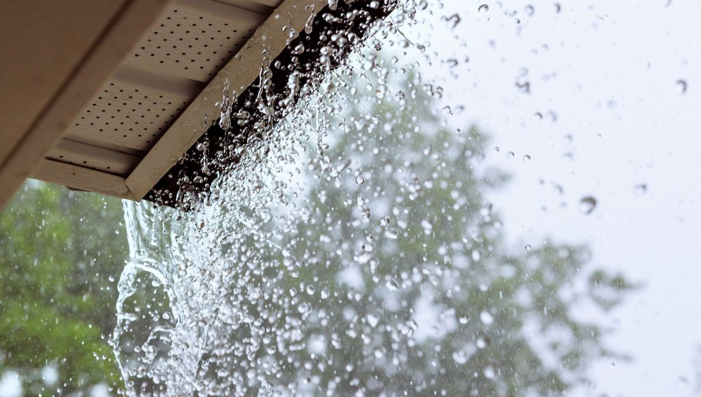 Rainwater gushing out of an overflowing gutter during a heavy monsoon rainstorm.