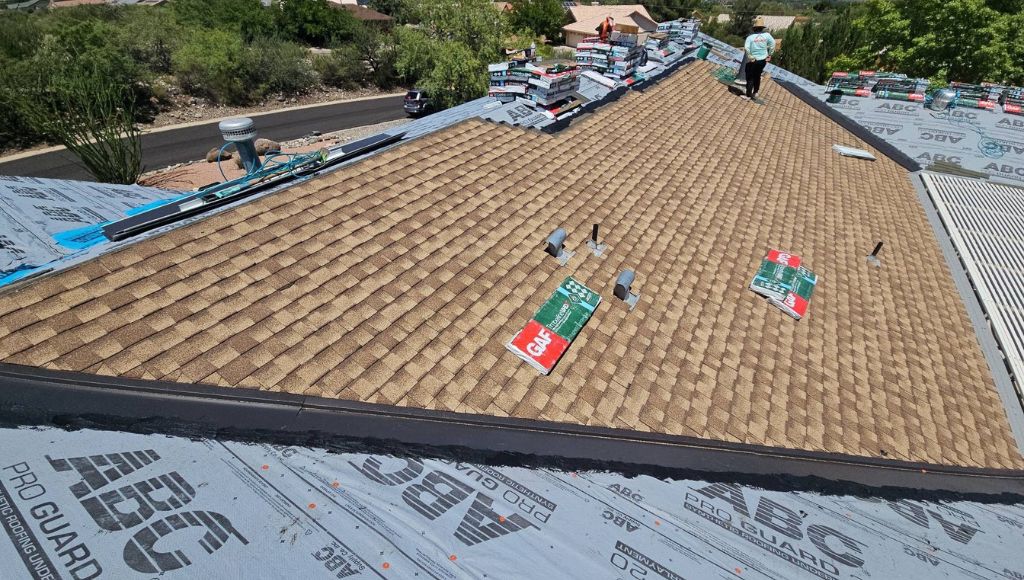 Professional roofers laying brand new, beige and light brown asphalt shingles on a residential roof.