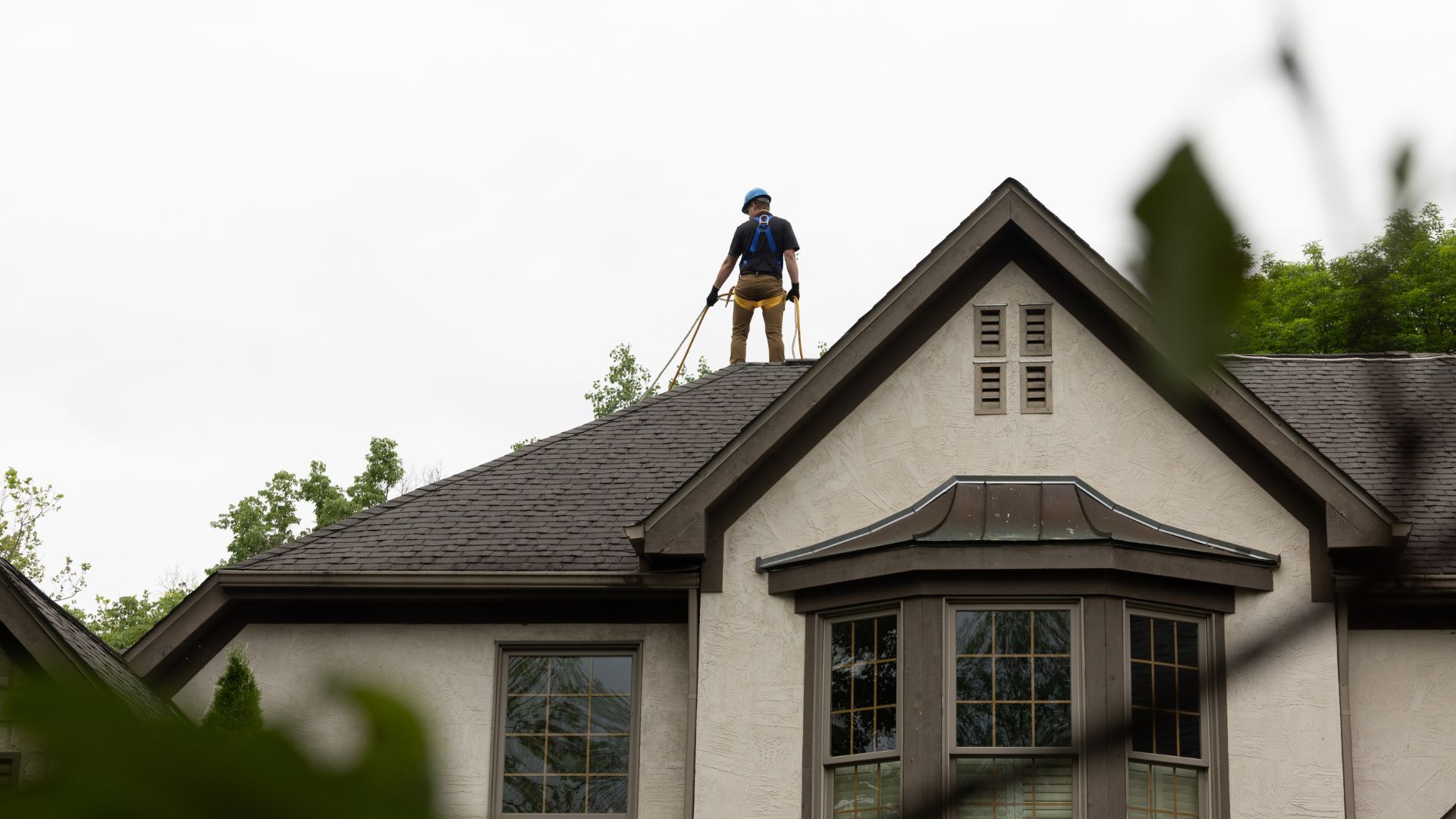 A professional roofer standing on a residential roof ridge in a full safety harness.