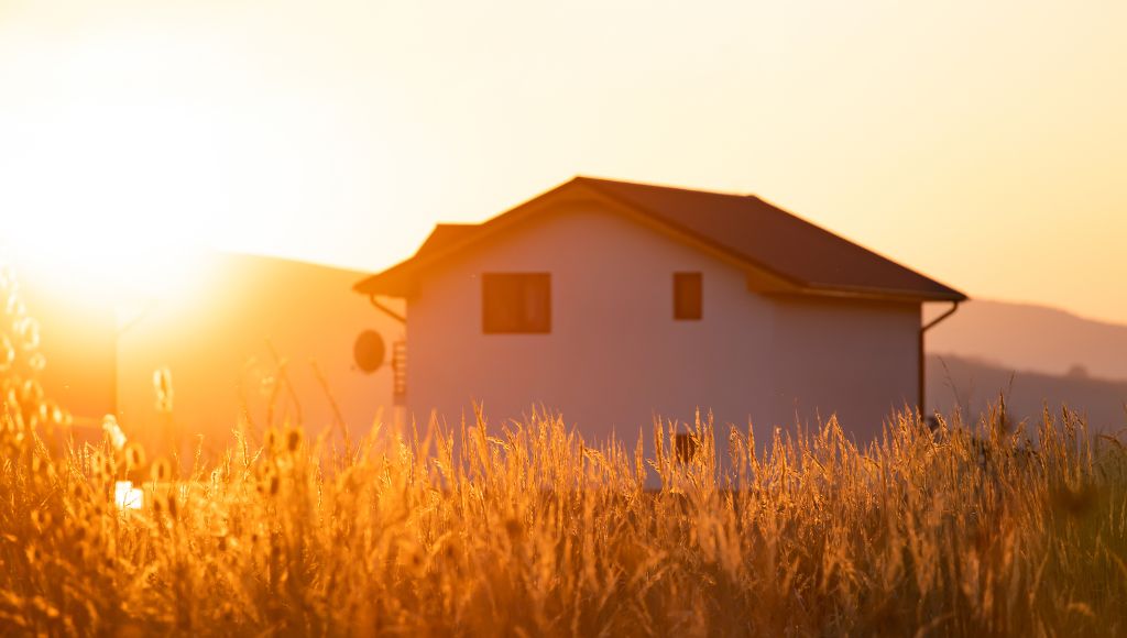 A hot desert sun rises over a residential house, exposing the roof to intense UV rays and heat.