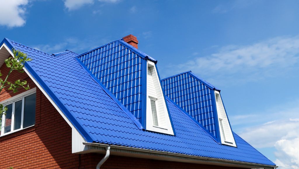 Close-up of a bright blue metal roof on a red brick house against a blue sky.