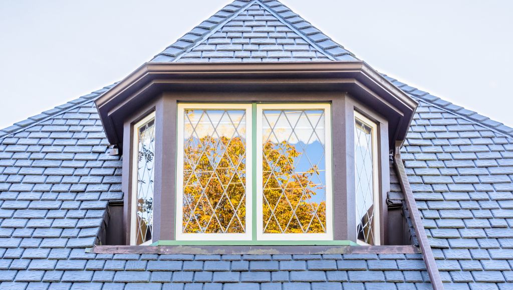 Close-up of a dormer window on a residential home with a roof covered in light blue-grey slate tiles.